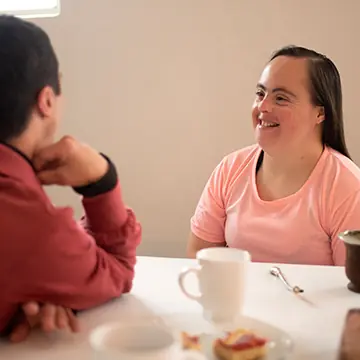 A woman talking with another person across a table in a home setting